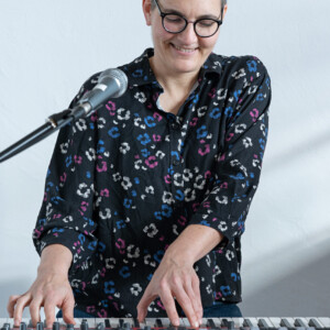 eine Person mit kurzen Haaren und Brille spielt Klavier